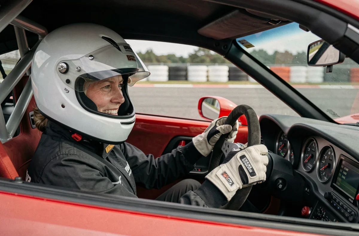Femme au volant d'une voiture de sport rouge sur circuit, portant un casque blanc et des gants de pilotage, concentrée sur la piste